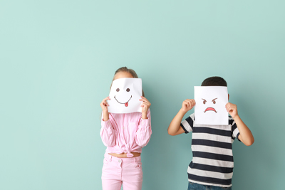 elearning provider in UK and Worldwide children learning to communicate their feelings with paper smiles and frowns being held in front of their faces
